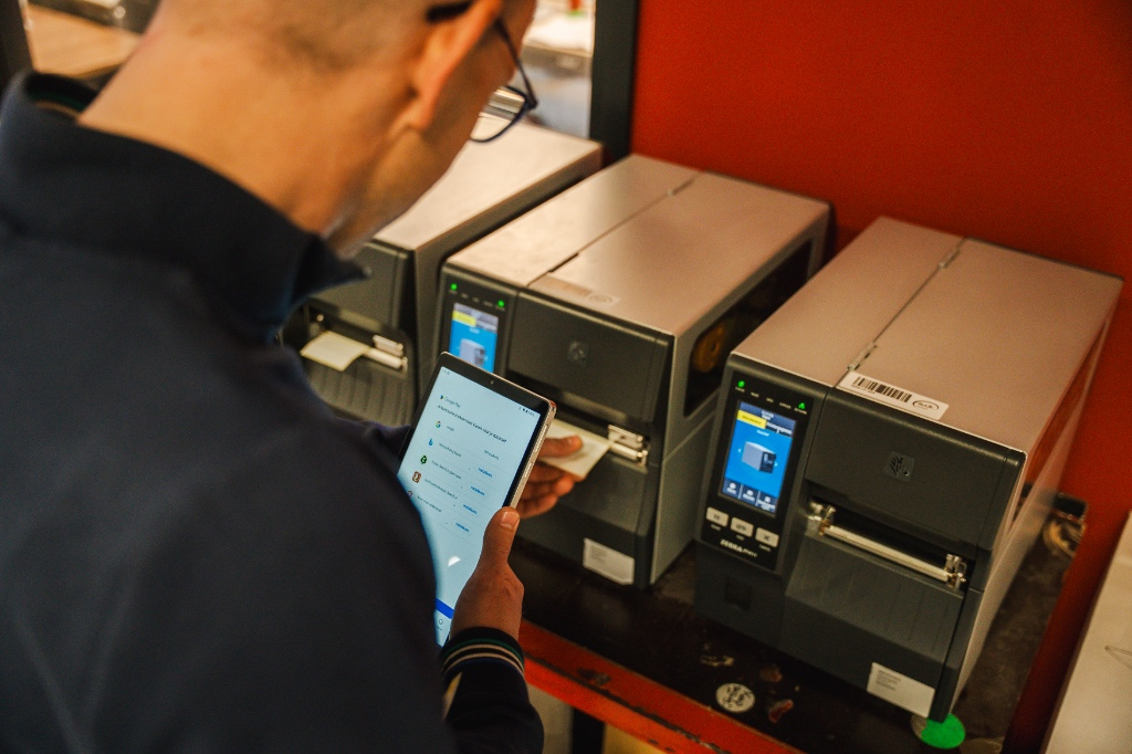 Medewerker met tablet bij labelprinters in een magazijn